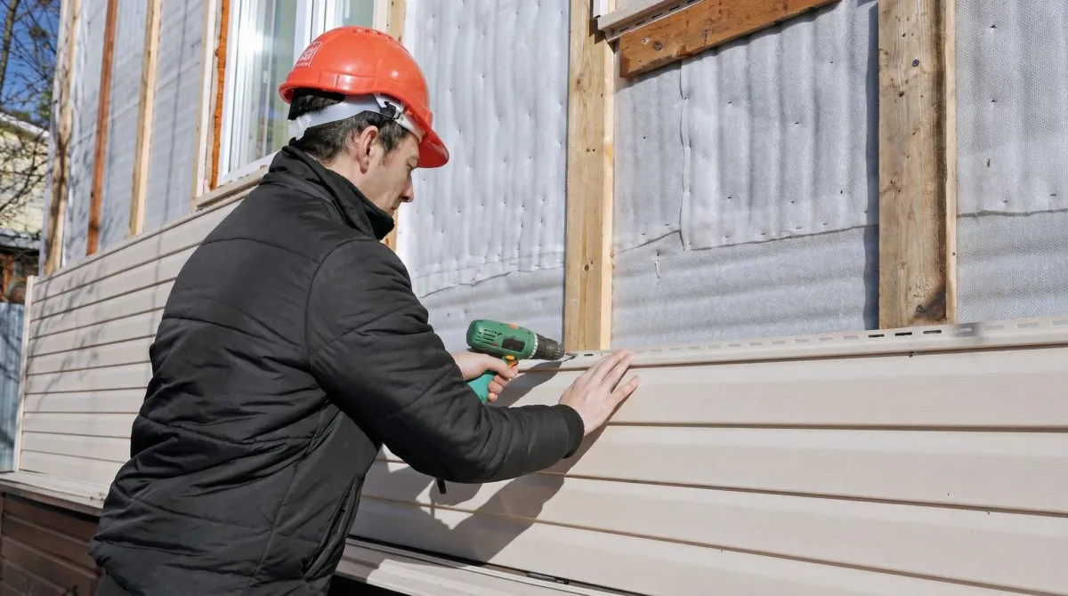 Siding replacement professional using a power drill to install new tan vinyl siding on a home exterior in Orlando, FL